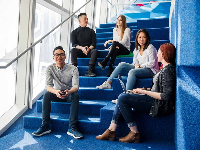 A group of students hanging out on the blue staircase in the Sandbox by DMZ in the SLC.