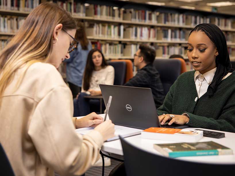 Two students studying at a table in the library.