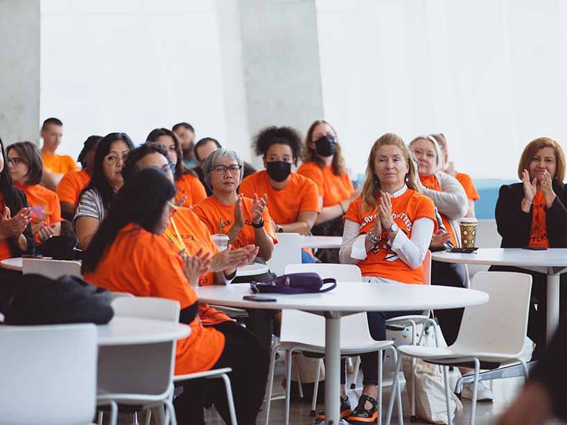 Community members in orange t-shirts sitting at round tables.