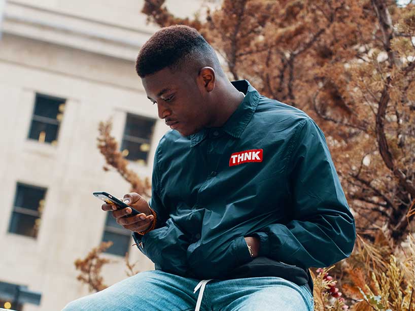 A young Black male sits outside looking at his phone on a fall day.