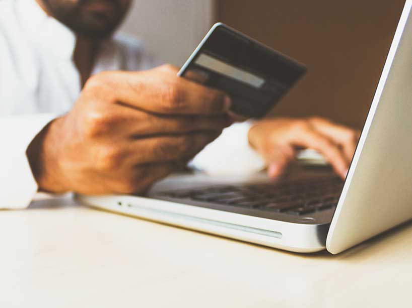 A man holds a credit card over a computer.