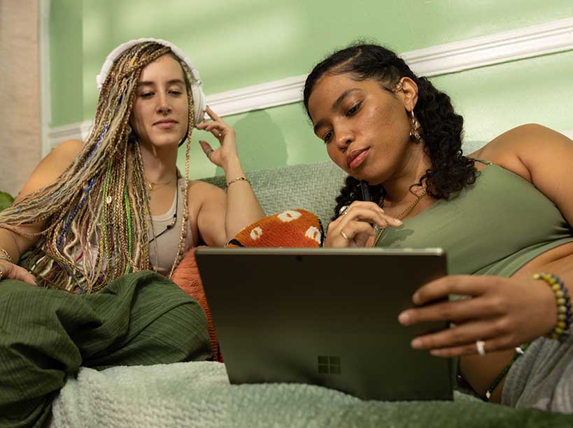 Two young women watch a laptop together.