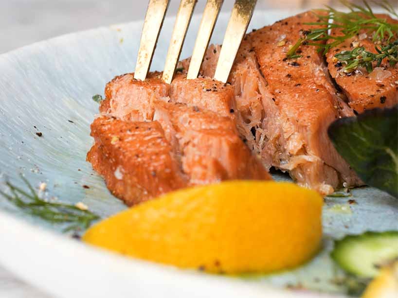 Photo of a plant-based seasoned salmon filet in a pan with vegetables around it.