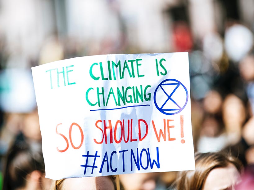 Someone holds up a sign in a crowd of people that says “The climate is changing. So should we.”