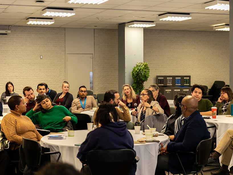 Community members sit around tables, engaged in discussion