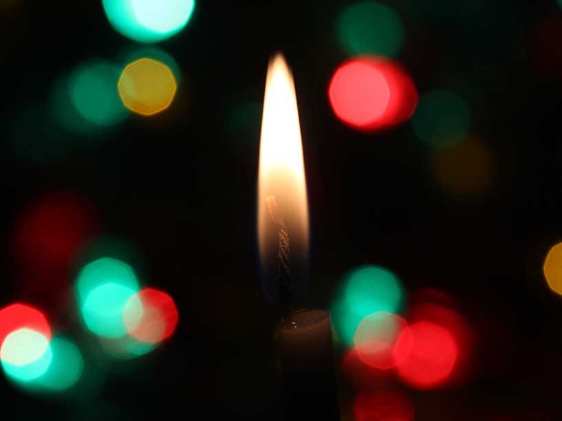 A candle flame burns, surrounded by red and green lights.