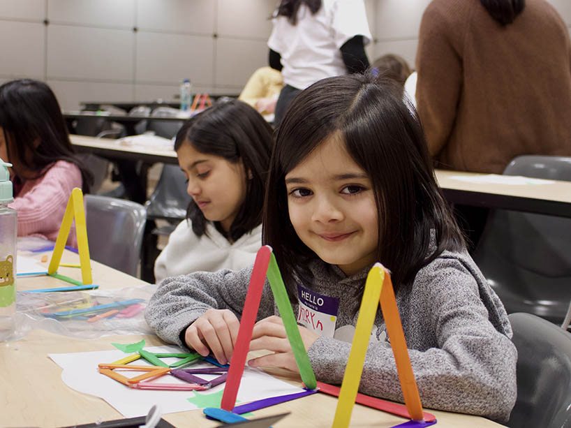 a young girl builds a ferris wheel out of coloured popsicle sticks