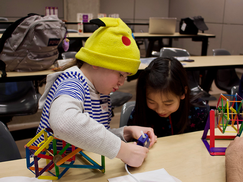 two young girls work together to put glue on a popsicle stick