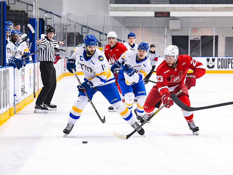 TMU Bold captain Chris Playfair, left, battles for the puck against an opposing player.