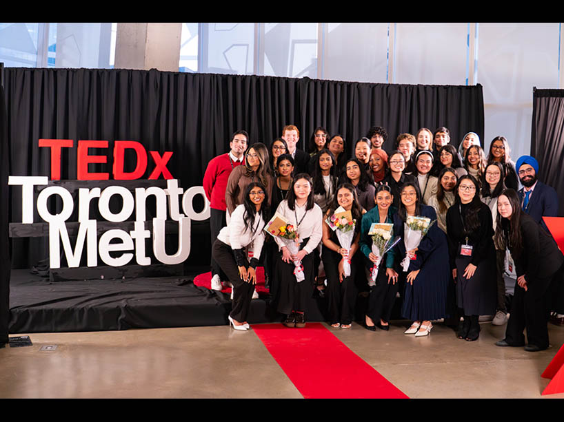 A group of people pose together by a “TEDxTorontoMetU” sign.