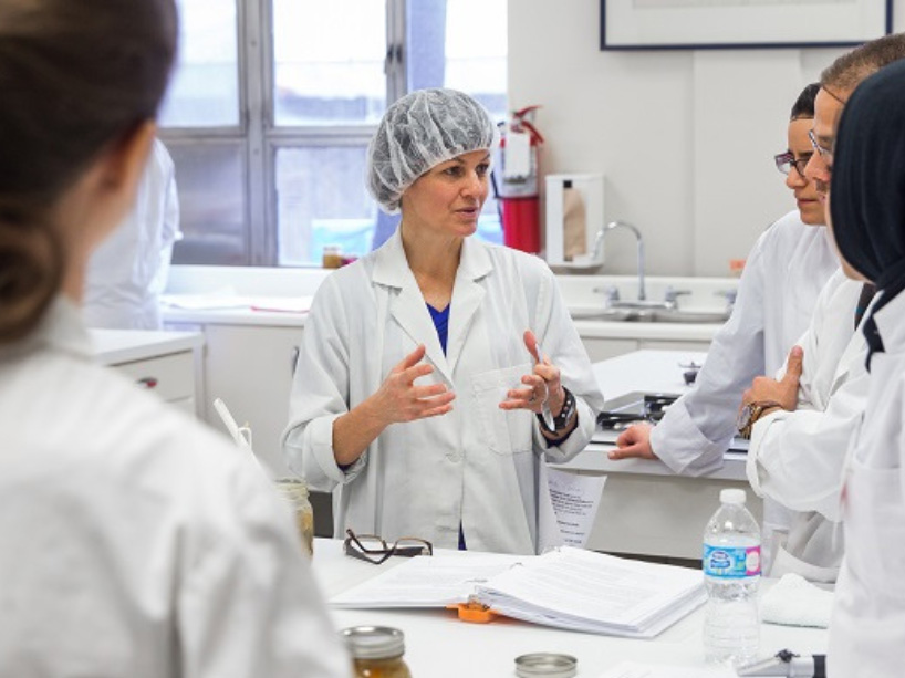 Janet Deacon in a food lab, she’s wearing a hair net and a white lab coat