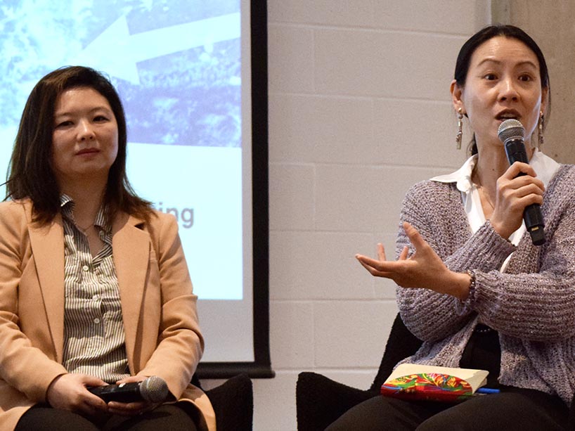 Zhixi Zhuang speaking into a microphone sitting next to Cathy Yang Liu.
