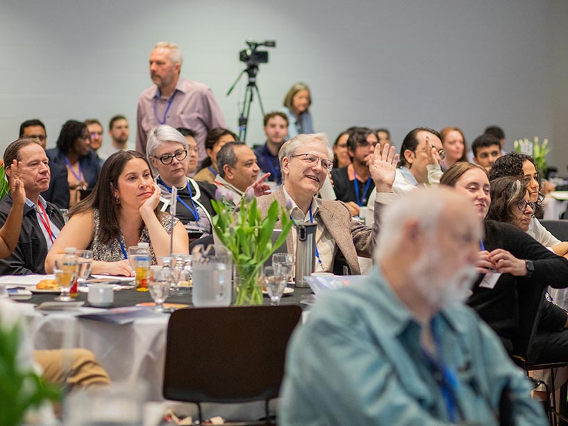 A group of people sitting around tables as some have their hands raised.