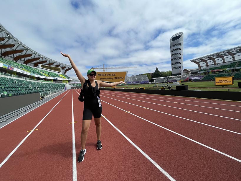 Sarah Jenkins stands on a track in a stadium with her arms extended over her head, smiling.