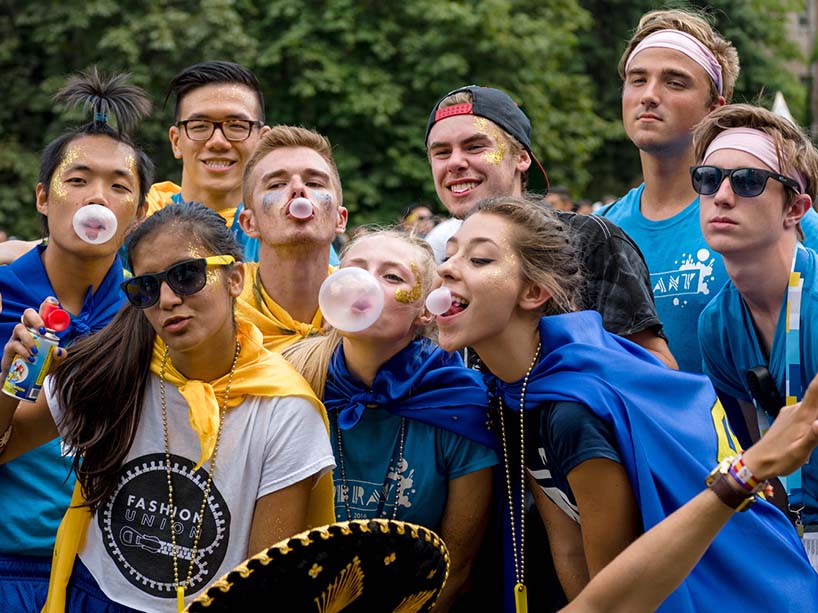 A group of young people wearing orientation week t-shirts blow bubble gum bubbles.