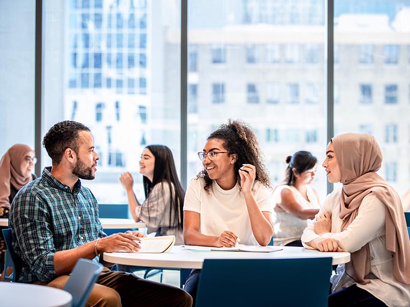 Three students from diverse backgrounds in discussion on the TMU campus.
