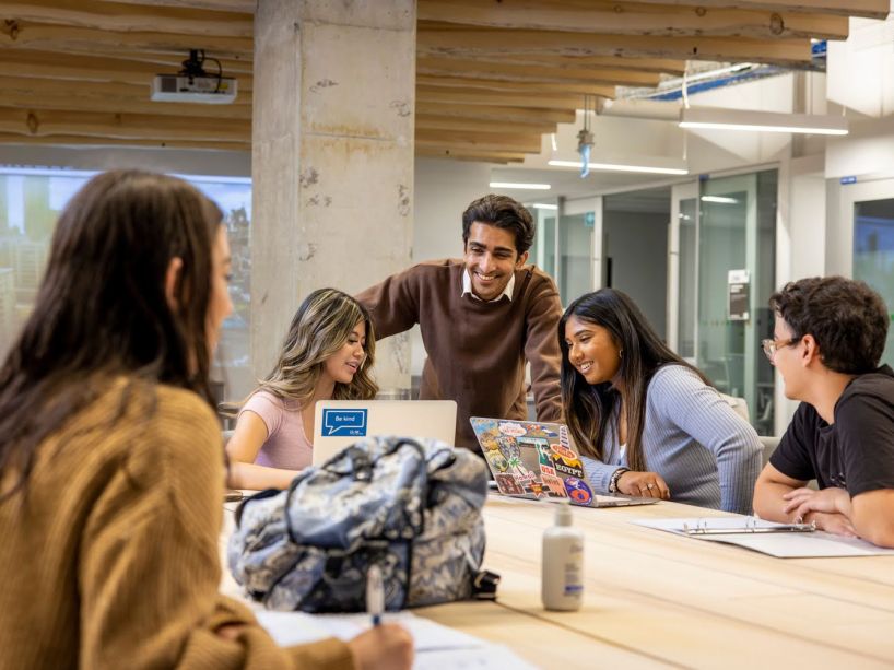 A group of five students working and talking in a common area 