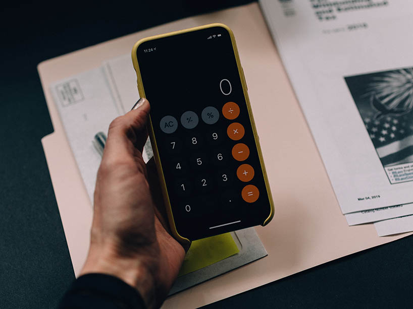A hand holds a calculator while looking at some documents. 