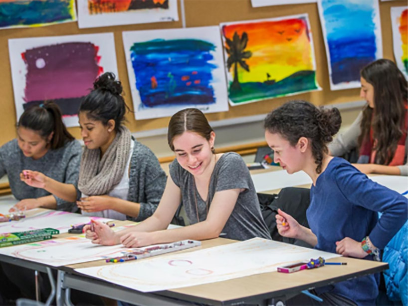 A group of students laughing together in an art class, surrounded by artworks on the walls.