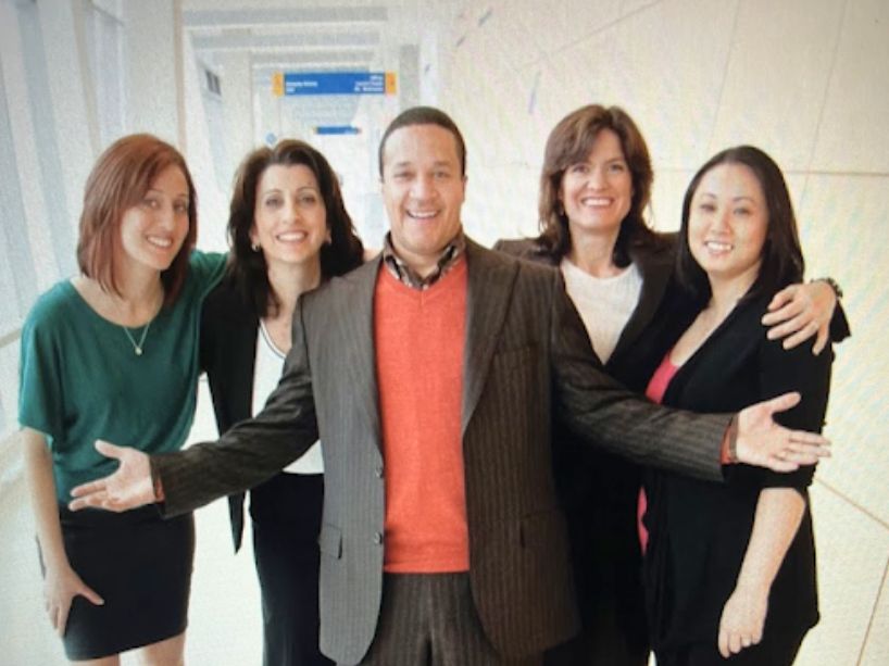 Five people wearing office attire pose for a photo. 