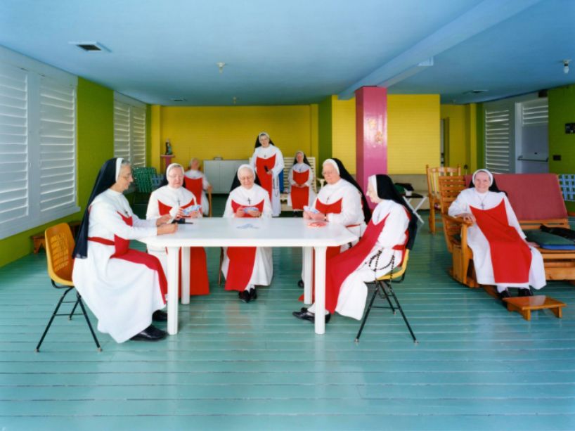  Nine nuns seated around a table, engaged in a game of cards, sharing a quiet, candid moment.