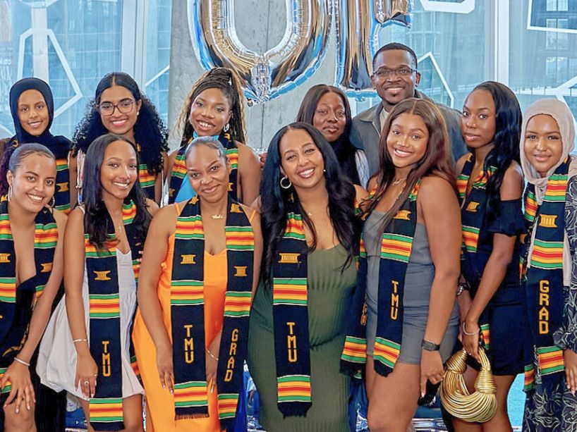  A group of graduating students standing in front of celebratory balloons, wearing Kente stoles. 