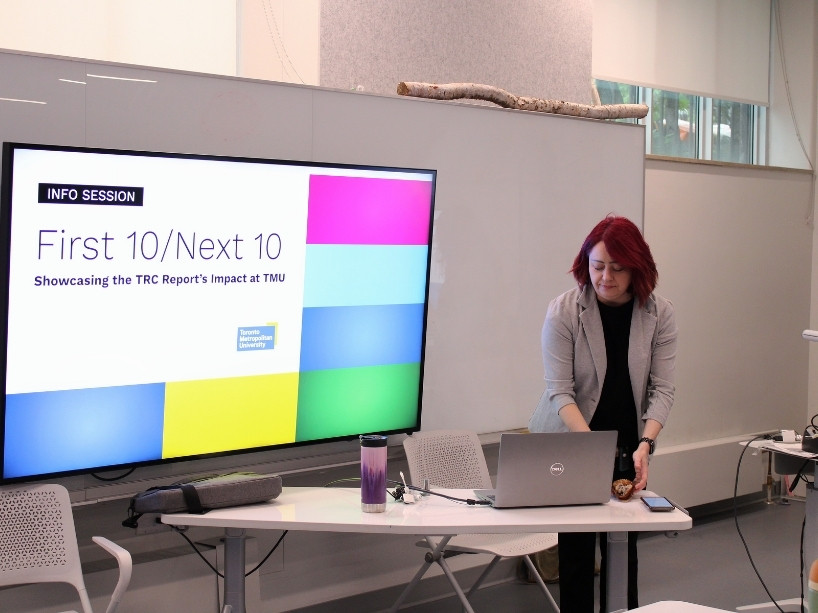 photo 1: Member from the National Indigenous Peoples Month/Orange Shirt Day Circle presents on a television Screen with a slide that reads “Info Session: First 10/Next 10: Showcasing the TRC Report’s Impact at TMU”
