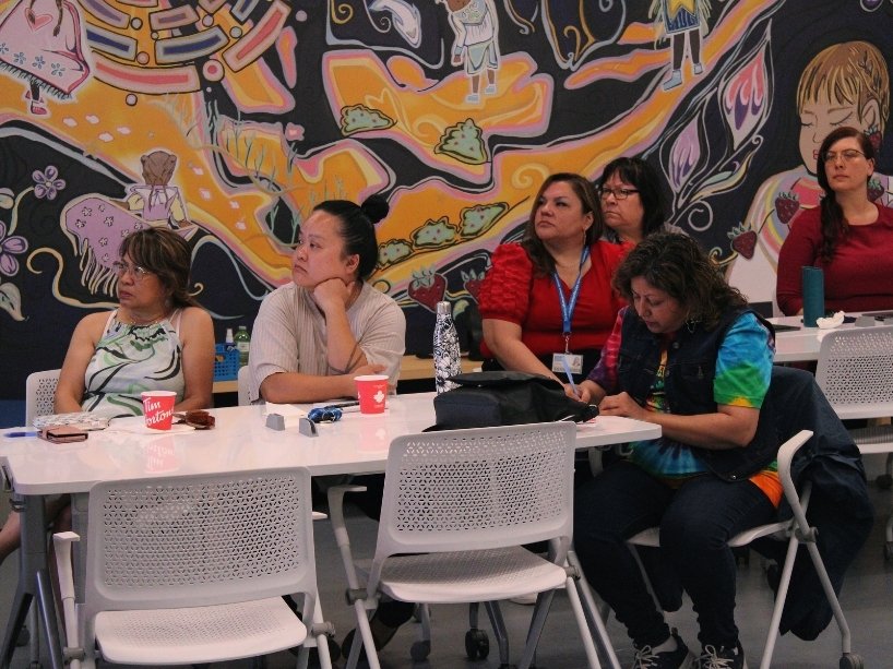 Community members sitting at a table watching the First 10/Next 10 Info session presentation.