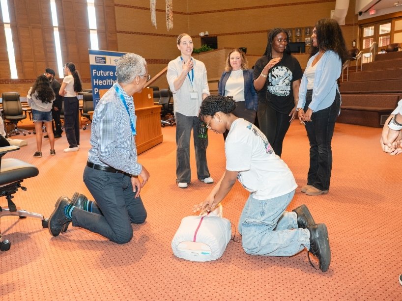 Dr. Shelton instructs highschoolers on CPR techniques as one student practices chest compressions on a mannequin.