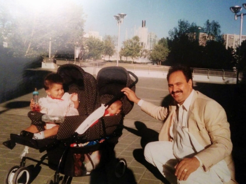 Baby Shabnam and her sister sitting in a stroller, with their father beside them, smiling.