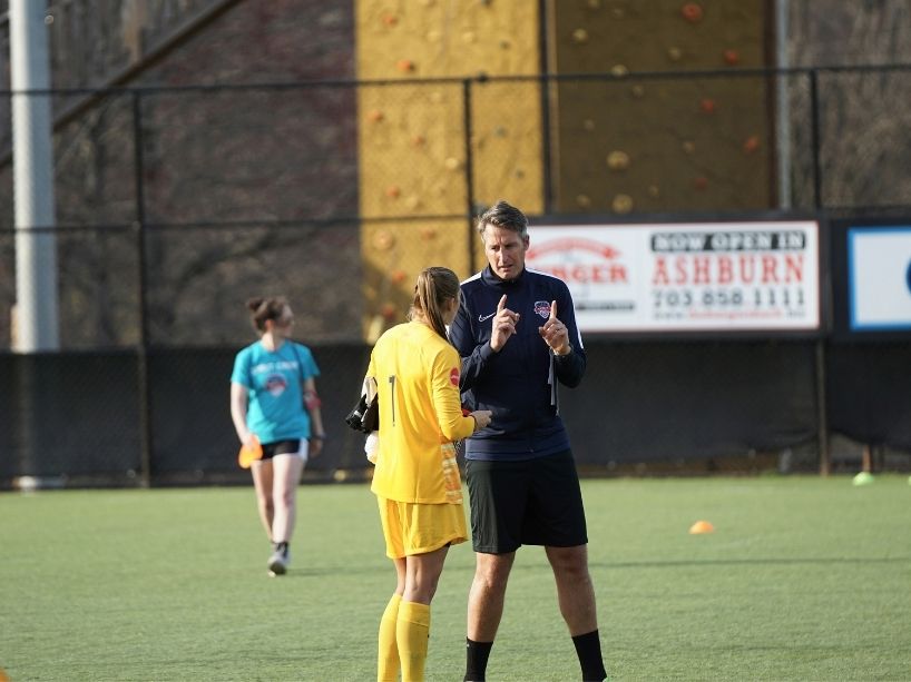 A female soccer player talks with a coach on the field.