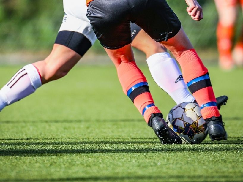 Two male soccer players kicking a ball between them on the field. 