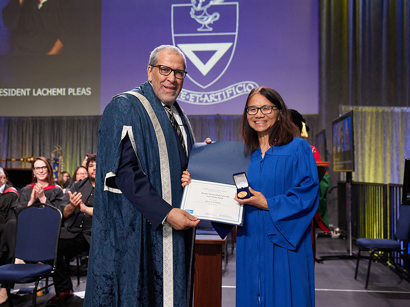 Two people wearing academic regalia pose for a photo with a certificate and a medal.