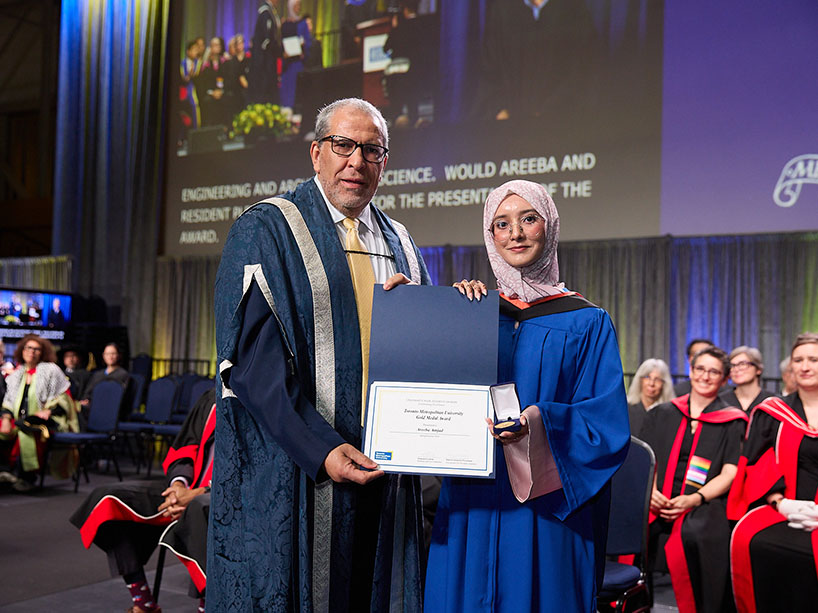 Two people wearing academic regalia pose for a photo with a certificate and medal.