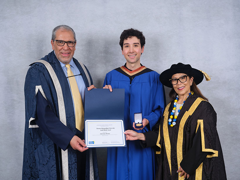Three people wearing academic regalia pose for a photo with a certificate and medal.