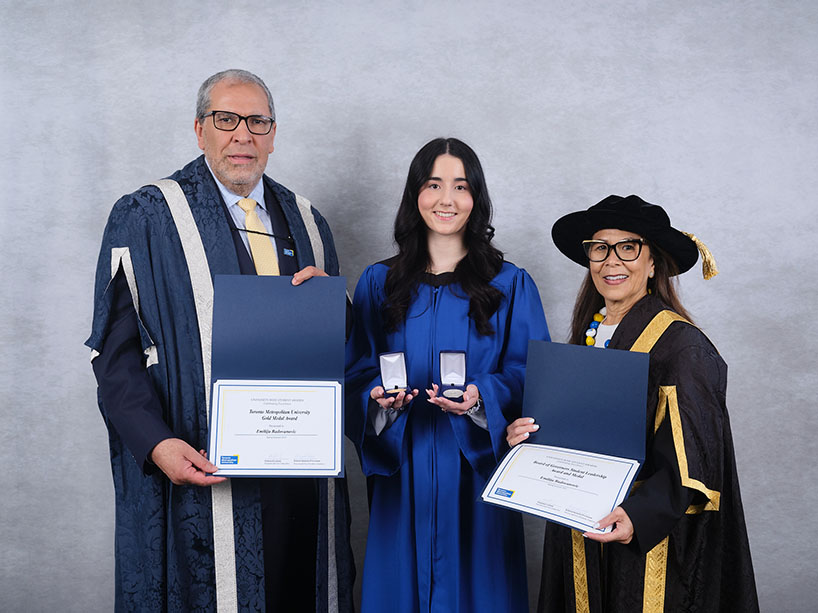 Three people wearing academic regalia pose for a photo with certificates and medals.
