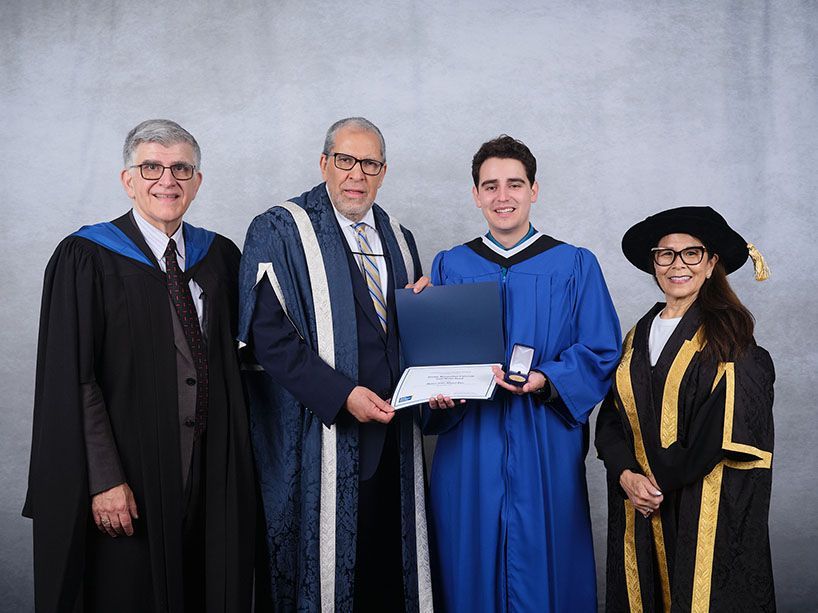 Four people wearing academic regalia pose for a photo with a certificate and medal.