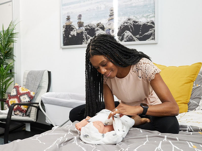 A woman attends to a realistic baby mannequin that is wrapped in a blanket.
