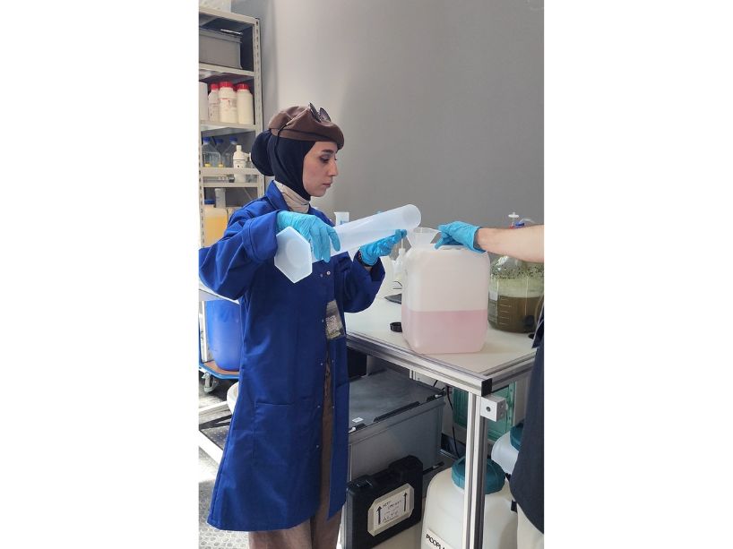 Allataifei pouring chemicals into a beaker in a lab at the Canada Pavilion in Venice while making the nutrition that maintains the living bacterial structure.