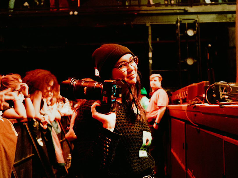 A teenager stands at the front of a crowd with a camera.