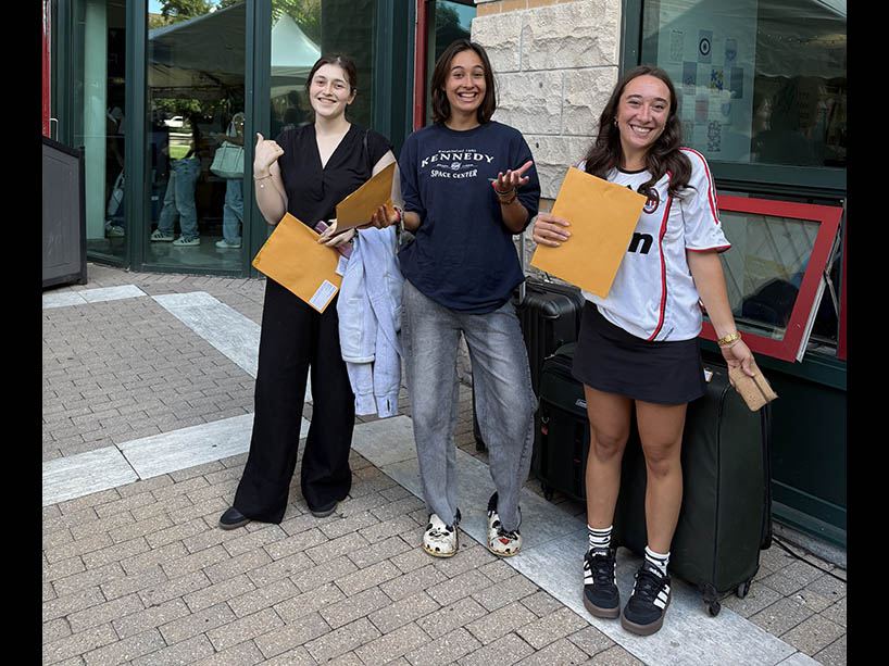 Three students holding envelopes smile for the camera.