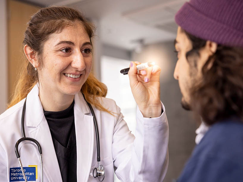 Nursing student checks student patient eyes with a pen light.