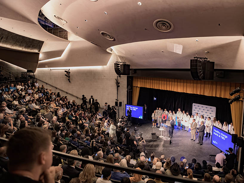 Individuals fill seats in a dimly lit auditorium as Premier Doug Ford speaks at the podium on stage. 