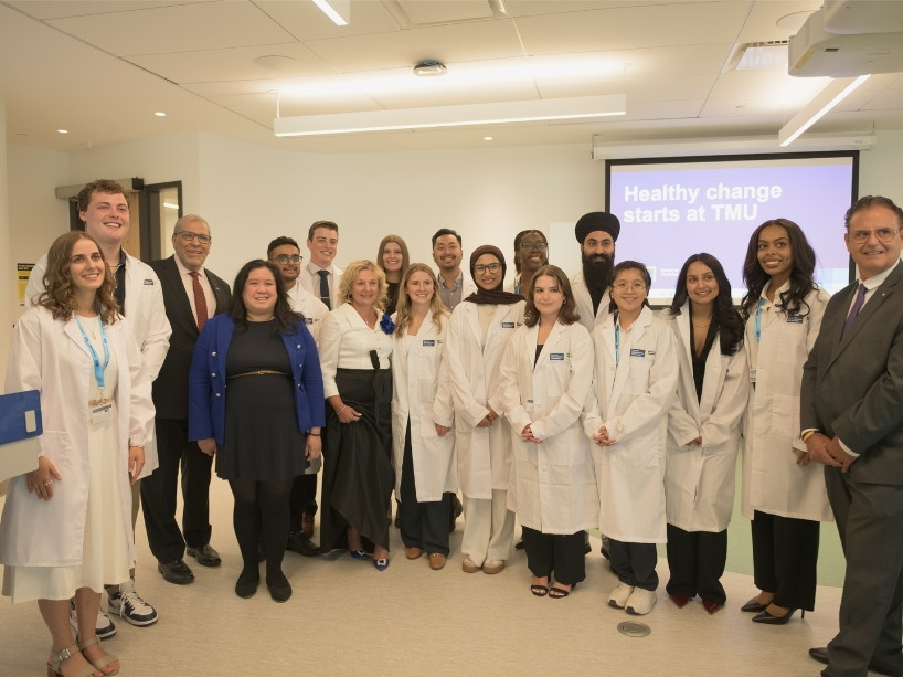 Students and TMU leaders standing in a classroom next to a teaching podium, smiling. 