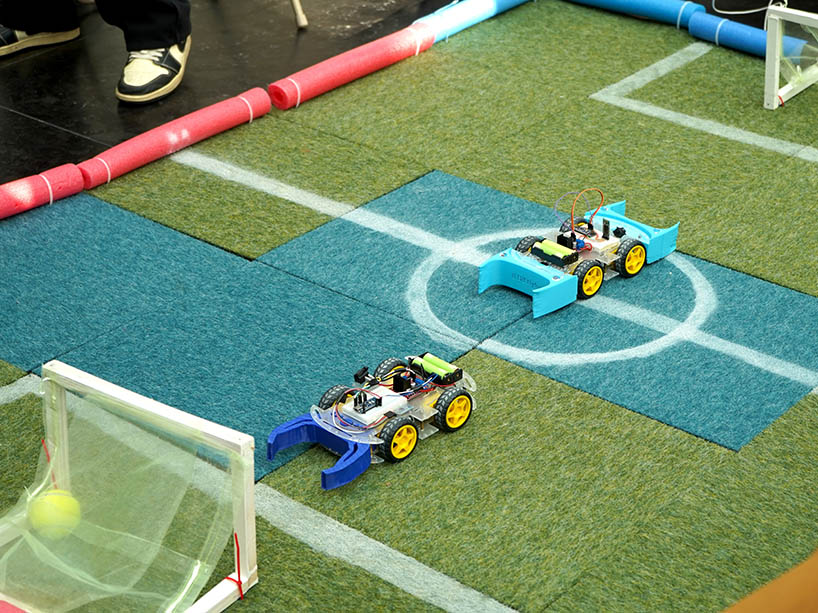 Two small robots on the pitch playing soccer. 