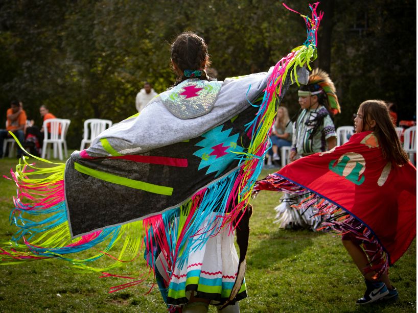 Shawl dancer in mid-movement with colourful shawl, decorated with ribbons, stretched out.