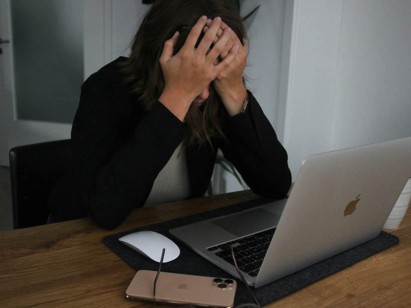 Person sitting at a laptop, holding their head in their hands.