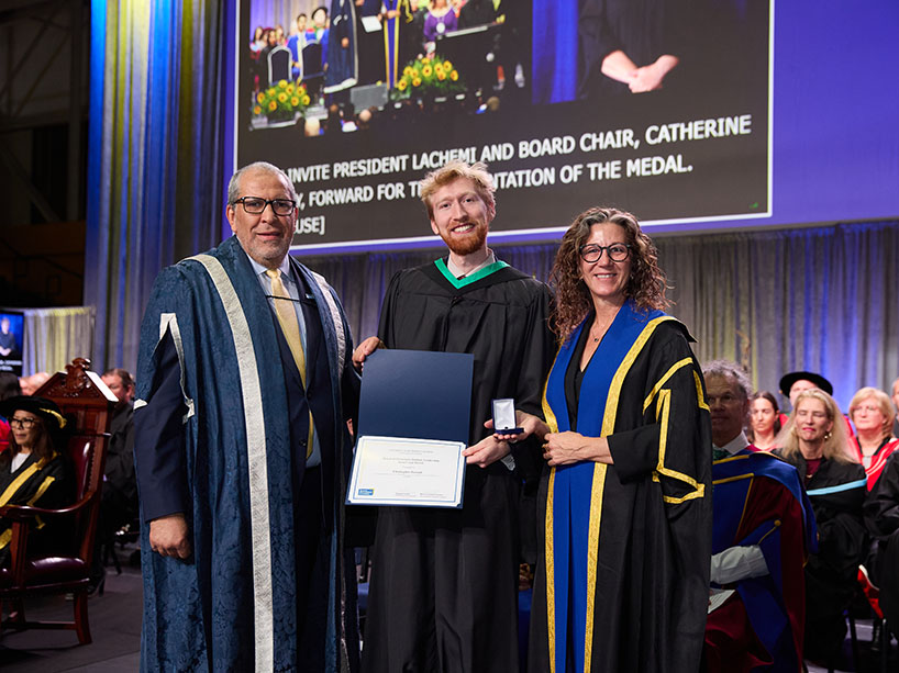 Three people in academic regalia pose for a photo.