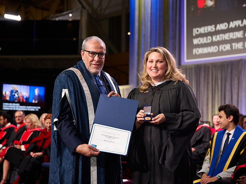 Two people in academic regalia pose for a photo.