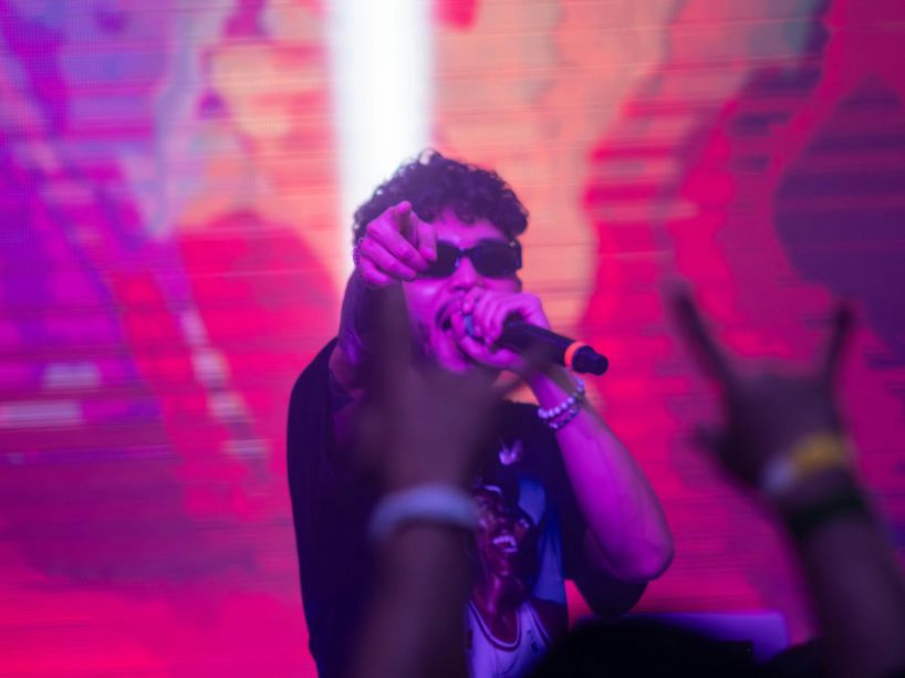 Male singer with sunglasses holds a microphone on a stage with pink lighting